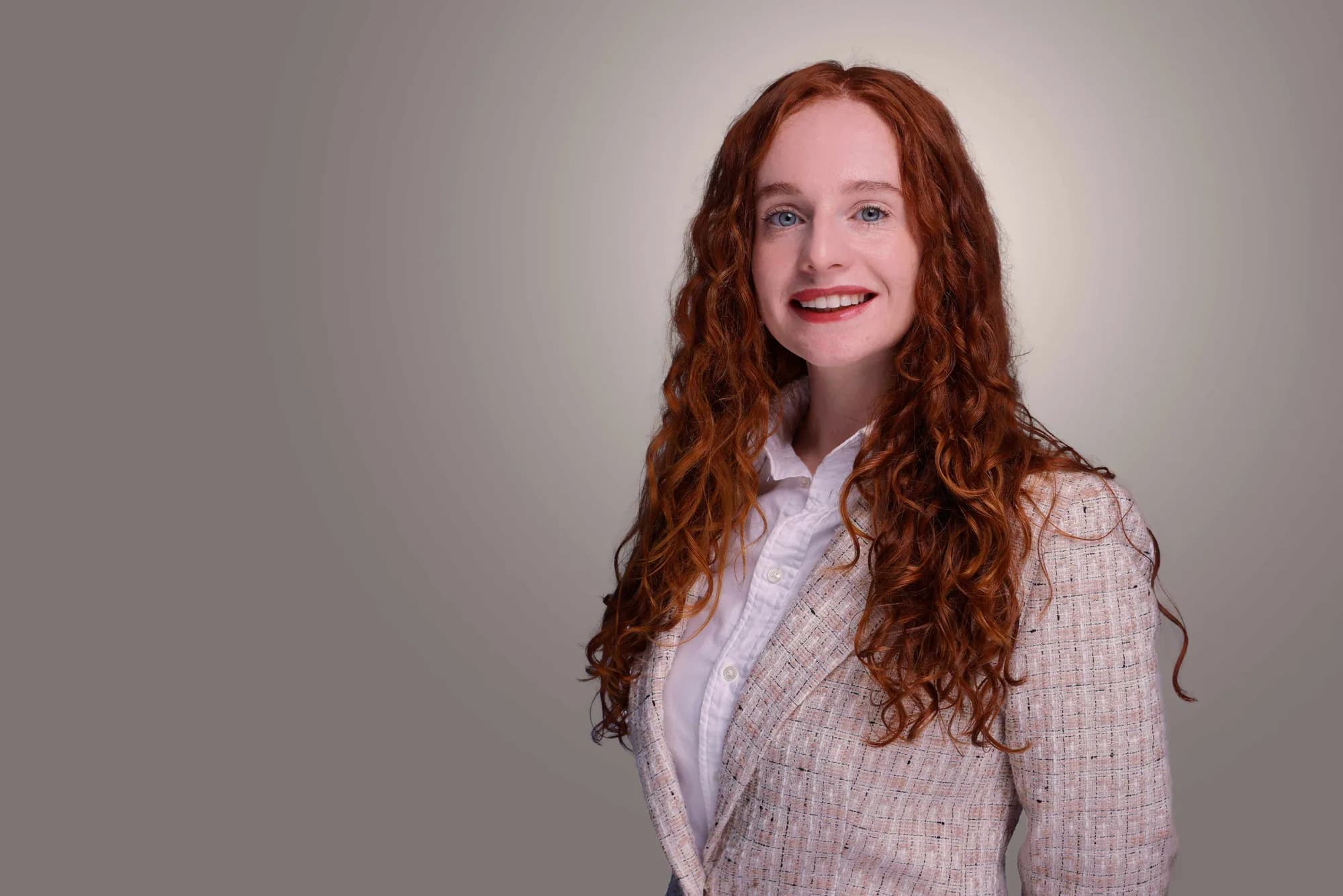 Corporate portrait of a woman with auburn hair on a soft grey backdrop