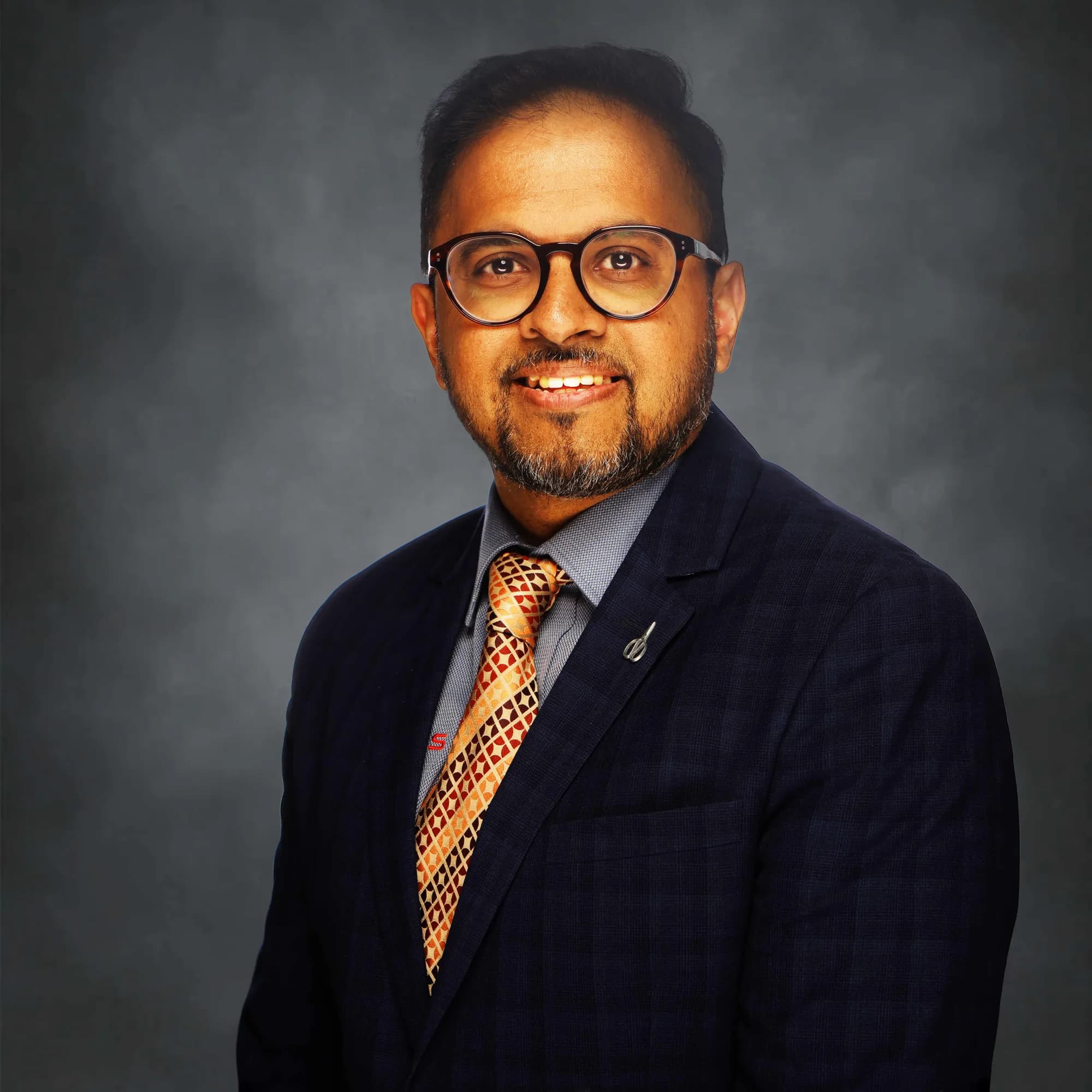 Corporate portrait of a man with an orange tie on a teal backdrop