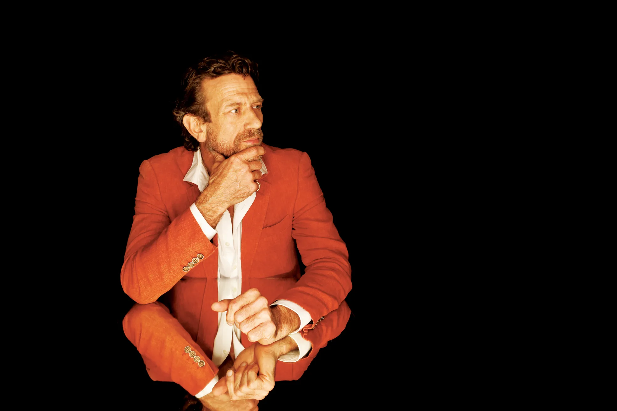 Editorial portrait of a man in a red jacket on a black background